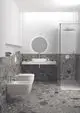 Badezimmer mit Wand-WC, Wandbecken und Dusche, umgeben von grauem Steinboden und -wänden. Runde Spiegelbeleuchtung. Produkte von Ideal Standard.
